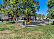 Thumbnail 15 of 20 - A playground with a red swing set and a blue roof is surrounded by a fence and a grassy area.