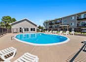 Thumbnail 17 of 20 - A swimming pool surrounded by white lounge chairs and a building in the background.