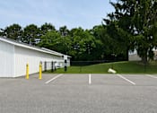 Thumbnail 14 of 26 - A parking lot with a white building and yellow bollards.