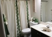 Thumbnail 14 of 31 - a bathroom with a white toilet next to a white sink with a green and white shower curtain