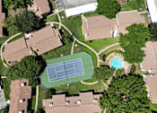 Thumbnail 24 of 30 - A tennis court is surrounded by houses and trees.