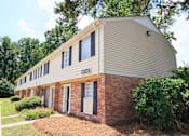 Thumbnail 15 of 17 - A house with a beige siding and a brick base with a white door and windows.