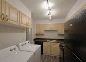 Thumbnail 4 of 11 - In-home washer and dryer in kitchen area with oven and a black refrigerator.