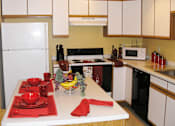 Thumbnail 2 of 19 - A kitchen with a white fridge, a white table with red napkin and red bowls.