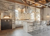 Thumbnail 14 of 24 - A modern kitchen with a stone fireplace and bar stools.