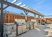 Thumbnail 19 of 24 - A row of outdoor kitchen appliances are lined up under a pergola.