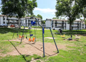 Thumbnail 16 of 18 - a swing set in a park with apartment buildings in the background