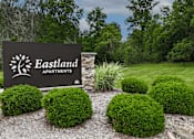Thumbnail 27 of 30 - A sign for Eastland Apartments is surrounded by green bushes.