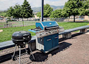 Thumbnail 22 of 30 - A blue grill is on a picnic table outside.