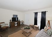 Thumbnail 4 of 23 - A living room with a grey couch, a wooden coffee table, and a television on a cabinet.