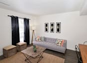 Thumbnail 1 of 23 - A living room with a grey couch, a wooden coffee table, and a black chair.