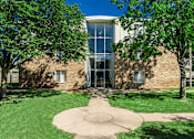 Thumbnail 7 of 8 - A building with a glass entrance is surrounded by trees.