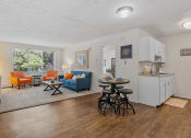 Thumbnail 8 of 25 - a living room with a couch a table and a chair and a kitchen with a sink and