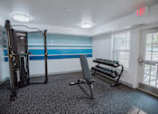 Thumbnail 16 of 37 - A gym room with a treadmill, weights, and a bench.