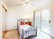 Thumbnail 10 of 16 - A bedroom with a bed, a ceiling fan, and a sliding glass door.