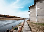 Thumbnail 10 of 18 - A wooden walkway runs alongside a body of water with a building on the right.