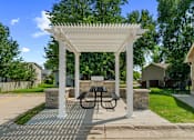 Thumbnail 12 of 26 - A white pergola with a table and chairs is set up in a park.