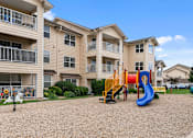 Thumbnail 21 of 29 - A playground with a blue slide and yellow climbing frame in front of apartment buildings.
