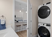Thumbnail 6 of 38 - A white washing machine is in a laundry room with a door open to a kitchen.