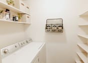 Thumbnail 15 of 25 - A white washing machine in a laundry room with shelves and storage.
