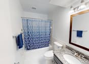 Thumbnail 9 of 32 - A bathroom with a white toilet, sink, and a blue shower curtain.