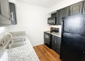 Thumbnail 3 of 24 - A kitchen with a black refrigerator, sink, and cabinets.