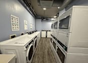Thumbnail 12 of 16 - A row of white washing machines in a laundry room.