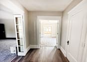 Thumbnail 18 of 32 - A hallway with a white door and a white cabinet with glass doors.