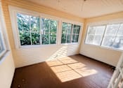 Thumbnail 25 of 32 - A sunny room with wooden floors and white walls.