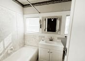 Thumbnail 24 of 32 - A white bathroom with a tub, sink, and mirror.