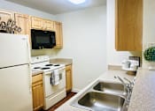 Thumbnail 6 of 18 - A kitchen with a white refrigerator, a black microwave, and a white oven.