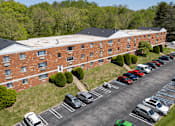 Thumbnail 24 of 25 - A parking lot with cars parked in front of a red brick building.