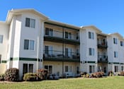 Thumbnail 6 of 6 - Apartment building with green bushes in front.