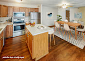 Thumbnail 3 of 6 - A kitchen with wooden cabinets and a dining table with chairs.