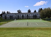 Thumbnail 14 of 18 - A tennis court is located in front of a large building.