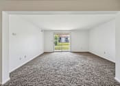 Thumbnail 8 of 34 - A large empty room with a carpeted floor and a view of a building through a window.