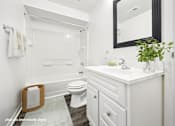 Thumbnail 5 of 34 - A white bathroom with a toilet, sink, mirror, and a potted plant.