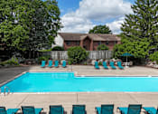 Thumbnail 24 of 35 - A pool surrounded by chairs and trees with a house in the background.