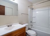 Thumbnail 8 of 20 - A white sink with a wooden cabinet and a white toilet in a bathroom.