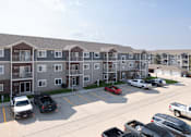 Thumbnail 26 of 29 - A parking lot in front of apartment buildings with cars parked.