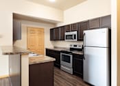 Thumbnail 1 of 29 - A kitchen with a white refrigerator, brown cabinets, and a granite countertop.