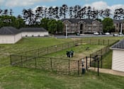 Thumbnail 16 of 33 - A tennis court is surrounded by a fence and a building is in the background.