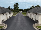 Thumbnail 15 of 33 - A long, straight road with a sidewalk on both sides and a row of garages on the right.
