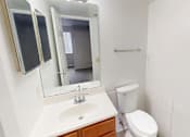 Thumbnail 13 of 23 - A white bathroom with a toilet, sink, mirror, and a towel bar.