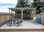 Thumbnail 9 of 11 - A wooden deck with a table and chairs under a pergola.