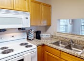 Thumbnail 4 of 35 - A kitchen with a white stove, wooden cabinets, and a granite countertop.