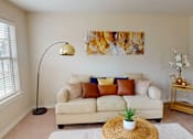 Thumbnail 6 of 35 - A living room with a white couch, a lamp, and a painting on the wall.