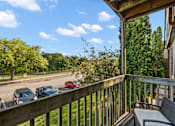 Thumbnail 10 of 31 - A balcony with a table and chairs overlooks a parking lot.