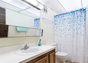 Thumbnail 5 of 8 - A white sink with a blue soap and a blue toothbrush in a bathroom with a white toilet and a shower curtain with blue dots.