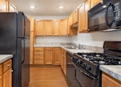 Thumbnail 2 of 8 - A kitchen with black appliances and wooden cabinets.